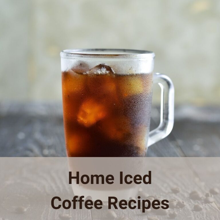 A glass mug of iced coffee on a rusticated wooden slate table top, and a few coffee beans scatter around the table. Here are a few iced coffee recipes.