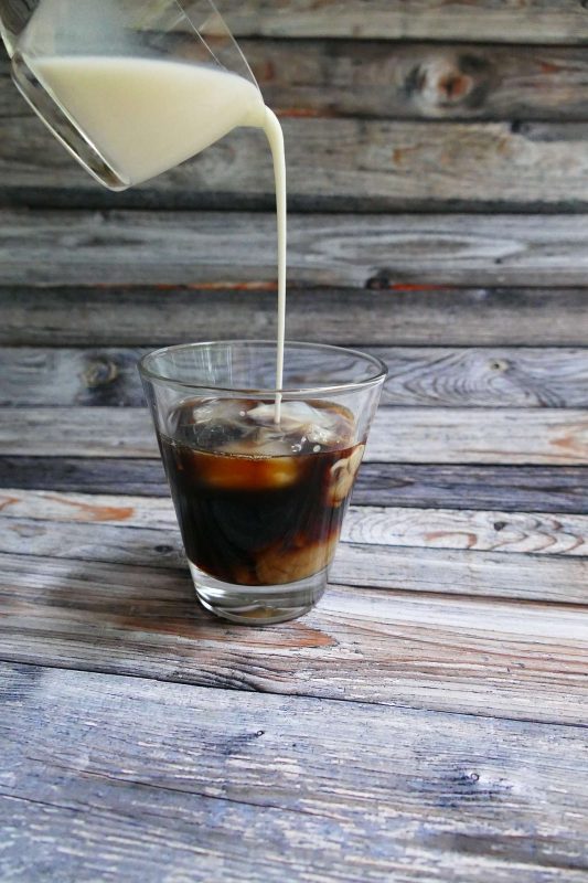 Milk is poured over a short glass of cold brew coffee on a rusticated slate table. I was able to make cold brew at home without any fancy equipment.