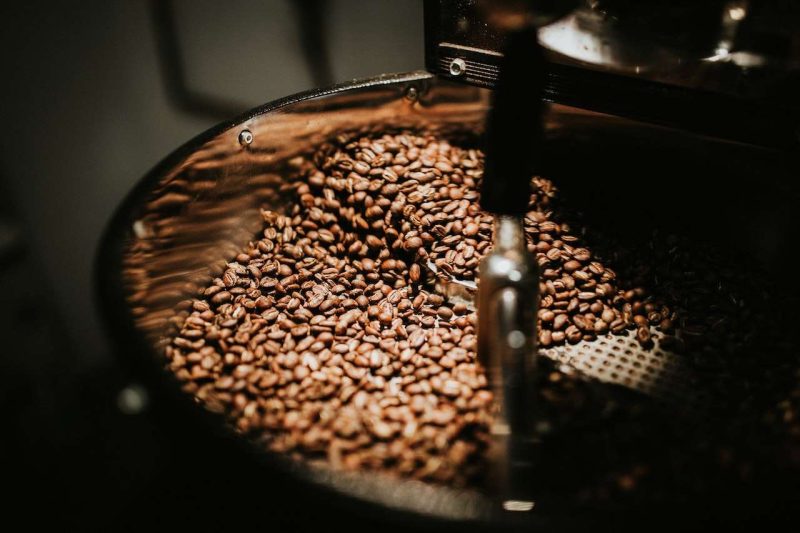 This photo shows a shiny metal coffee roaster is at work under dim light. Is coffee good for you? Coffee has protective effects against certain medical conditions.