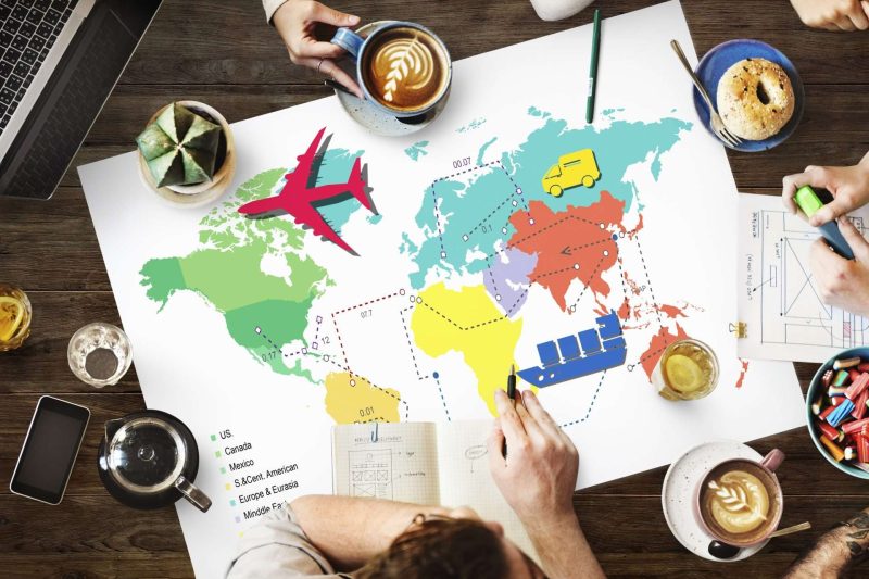 5 people sitting at a large table, drinking coffee. ice lemon tea, and eating bagel. A world map in diagram is in the middle of the table.