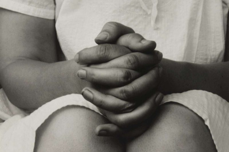 This is a black and white photo shot of a woman's hands are interlocked and resting on her knees. Only part of the white blouse and right arm can be seen in this close shot, so are her knees. It implies an anxious body language. Is coffee good for you? It may cause anxiety if you drink too much of it.